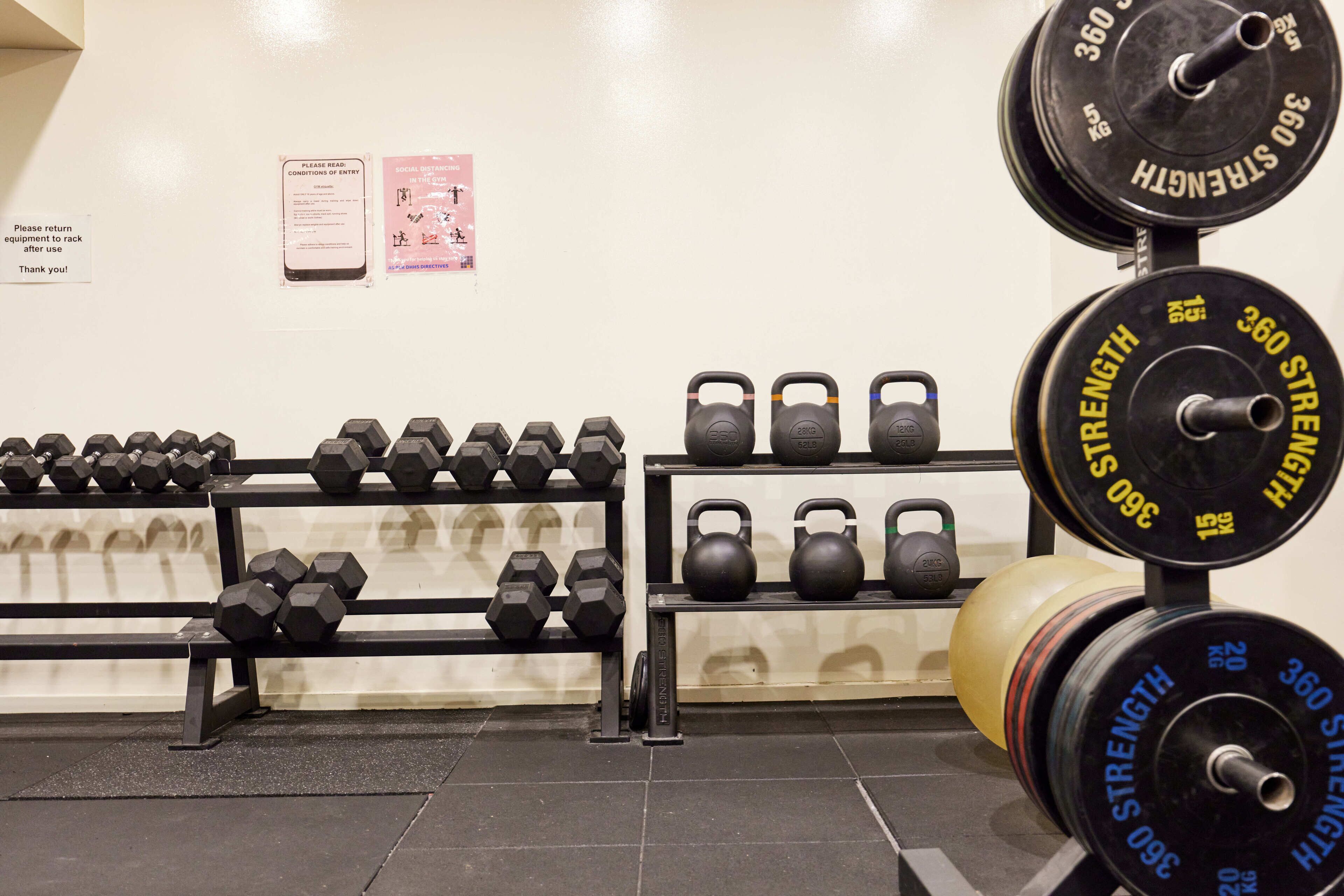 Une salle de sport équipée de matériel de musculation, notamment des haltères, des kettlebells et une barre avec des disques de poids.