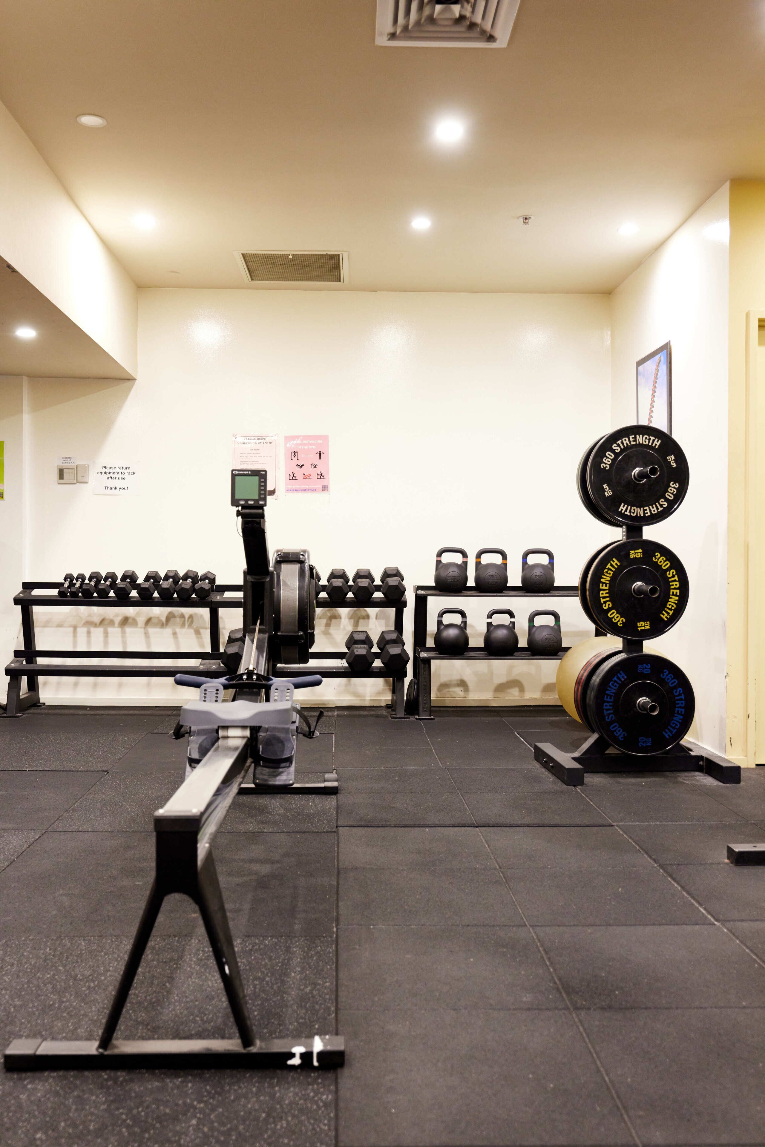 Uma academia com equipamentos de musculação, incluindo halteres, kettlebells e barras.