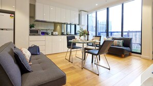 A modern kitchen with white cabinets, a dining area with a glass table, and a sofa with cushions.