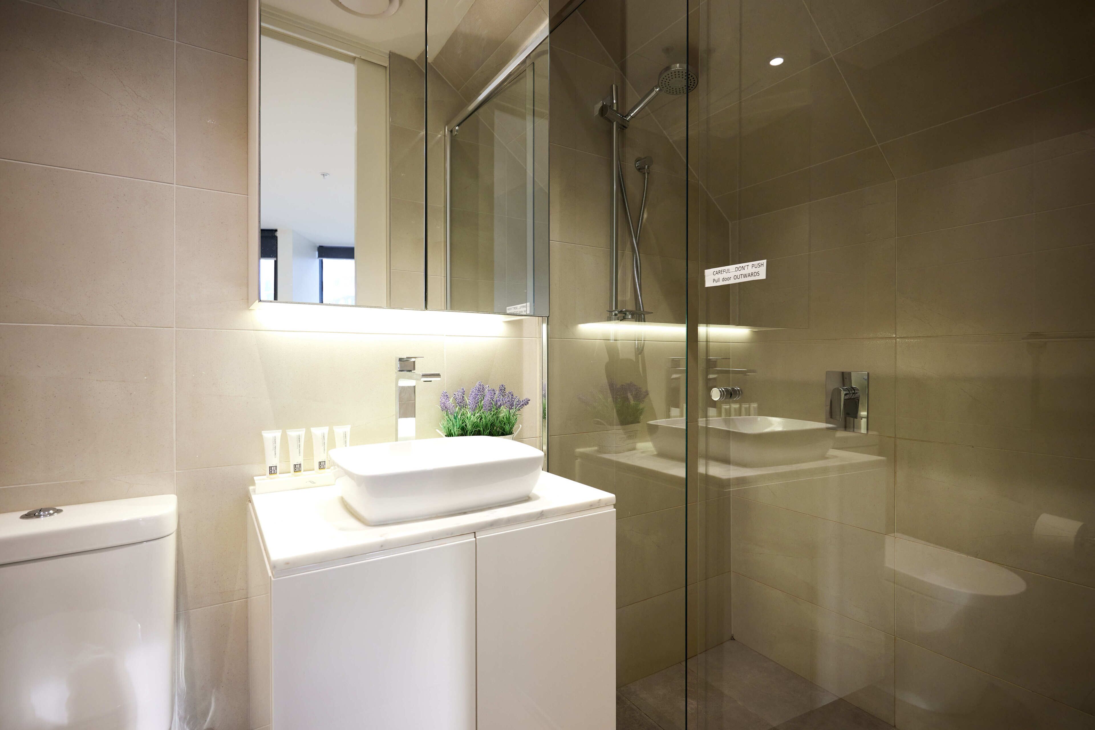 Un baño moderno con cabina de ducha de vidrio, un lavabo blanco con lavamanos integrado y un inodoro.