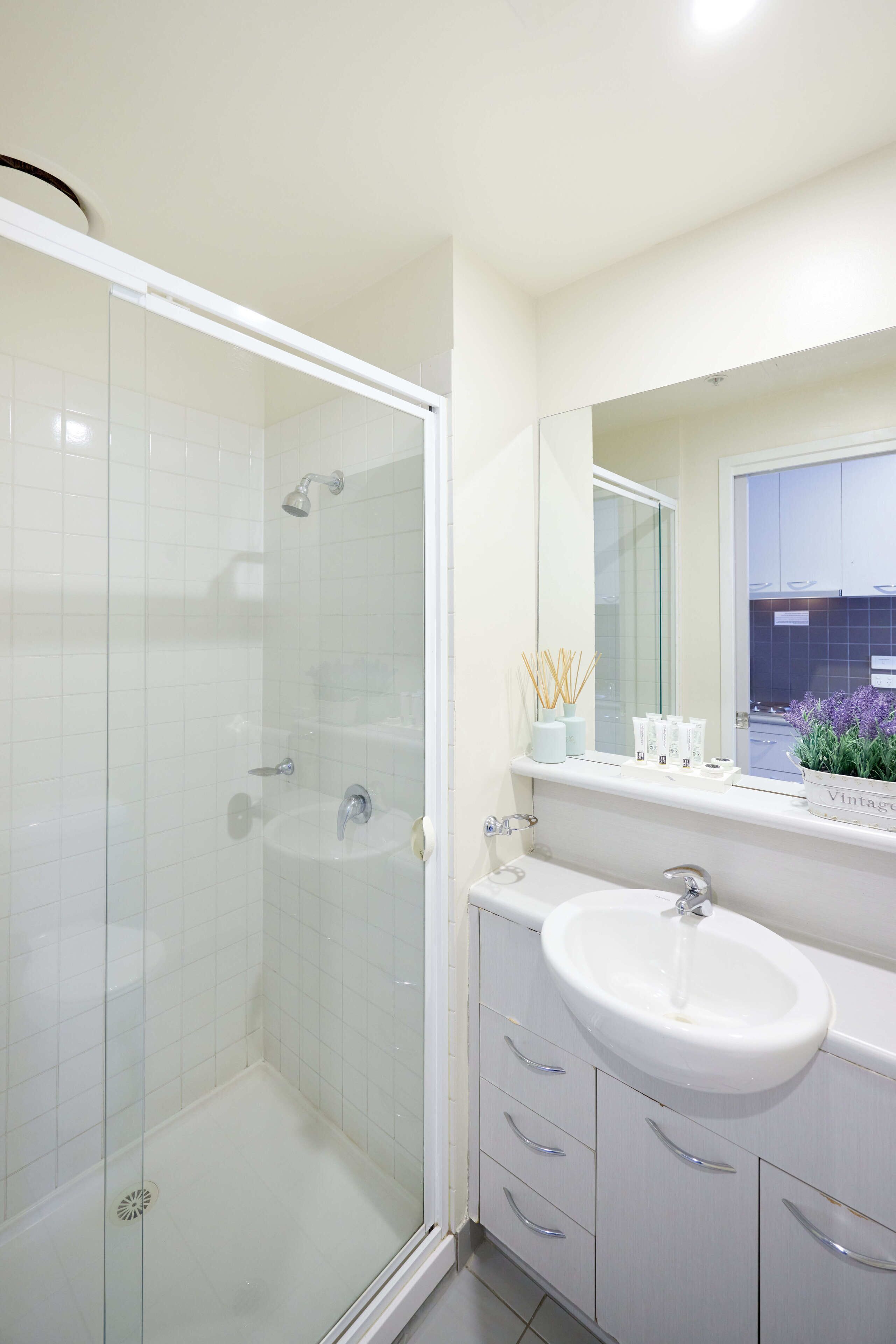Un baño moderno con ducha envuelta en vidrio, un lavabo blanco y un mueble de tocador con cajones.
