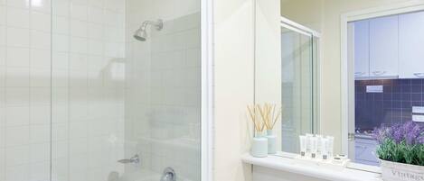 Un baño moderno con ducha envuelta en vidrio, un lavabo blanco y un mueble de tocador con cajones.
