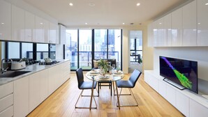 A modern kitchen with white cabinets, a dining table set for four, and a large TV on the wall.