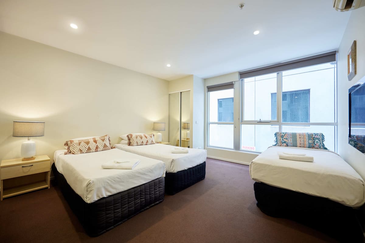 Una habitación de hotel con dos camas, un ventanal grande y una mesita de noche con lámpara.