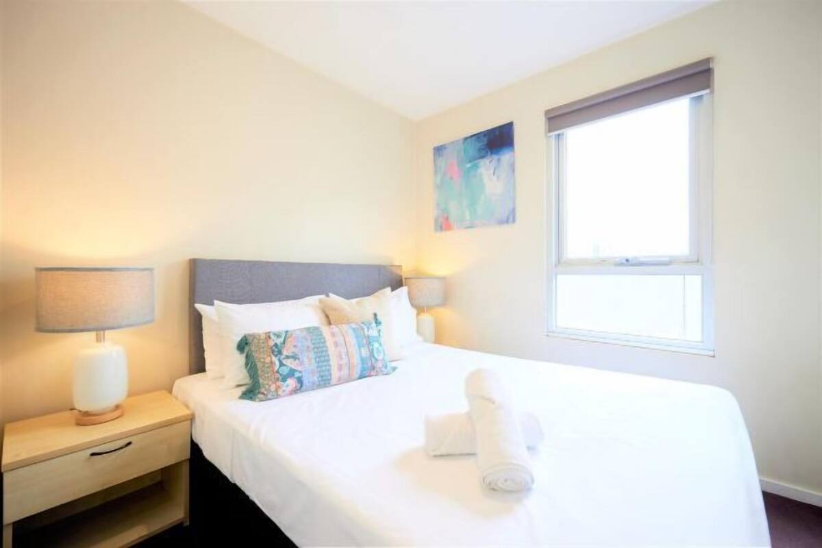 Habitación de hotel con cama, mesita de noche, lámpara, ventana y un cuadro en la pared.