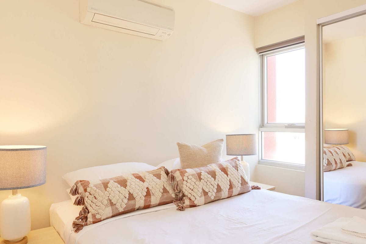 Una habitación de hotel con una cama grande, dos lámparas de noche, una ventana y un equipo de aire acondicionado.