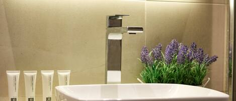 A modern bathroom with a large vessel sink, a mirror, and a potted lavender plant.