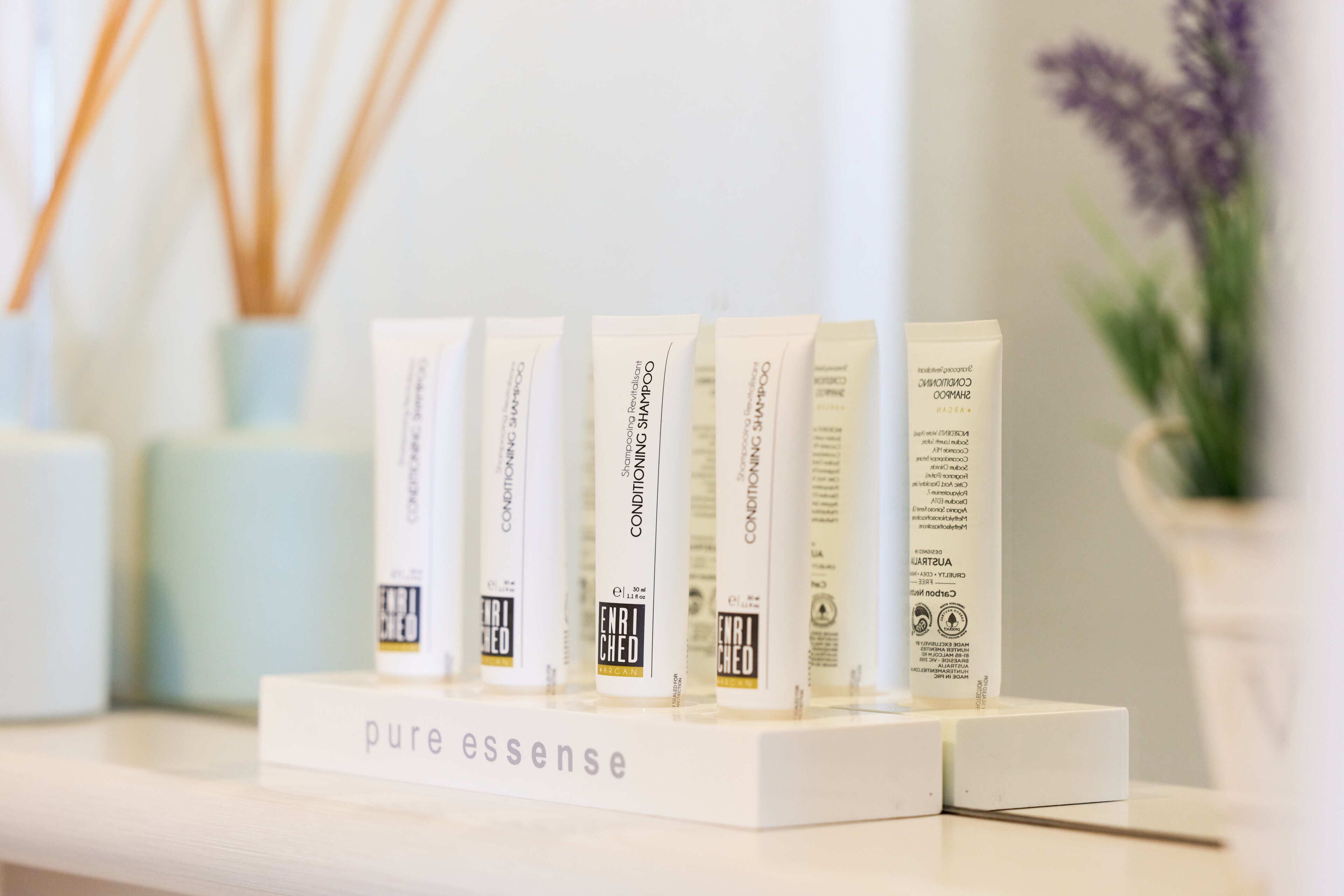 A display of 'pure essence' hair care products on a white shelf.