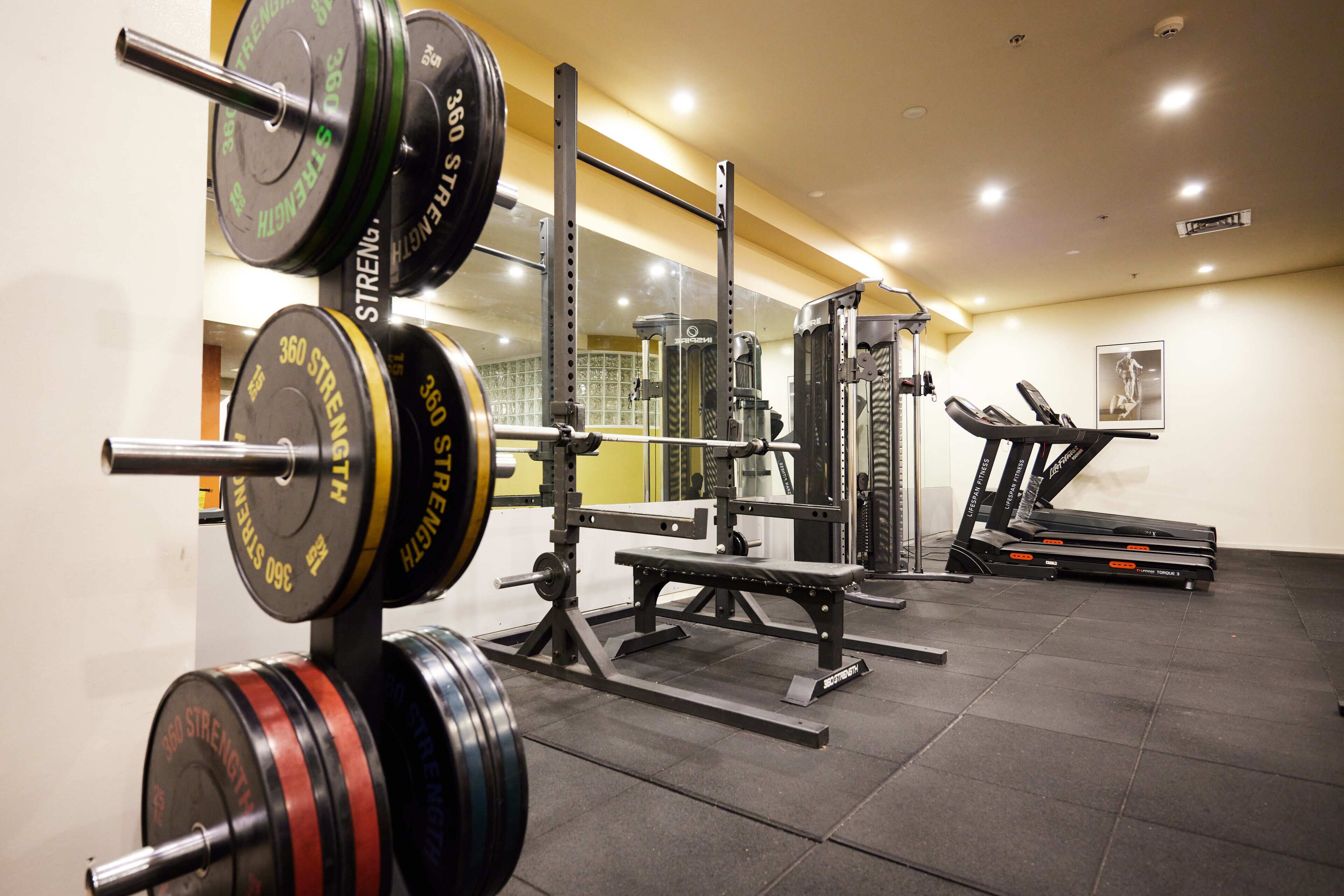 Une salle de sport équipée de matériel de musculation, de tapis de course et d’un miroir.