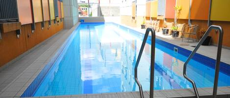 Une piscine intérieure à l’eau d’un bleu limpide, entourée de murs et d’un sol recouverts de carreaux.