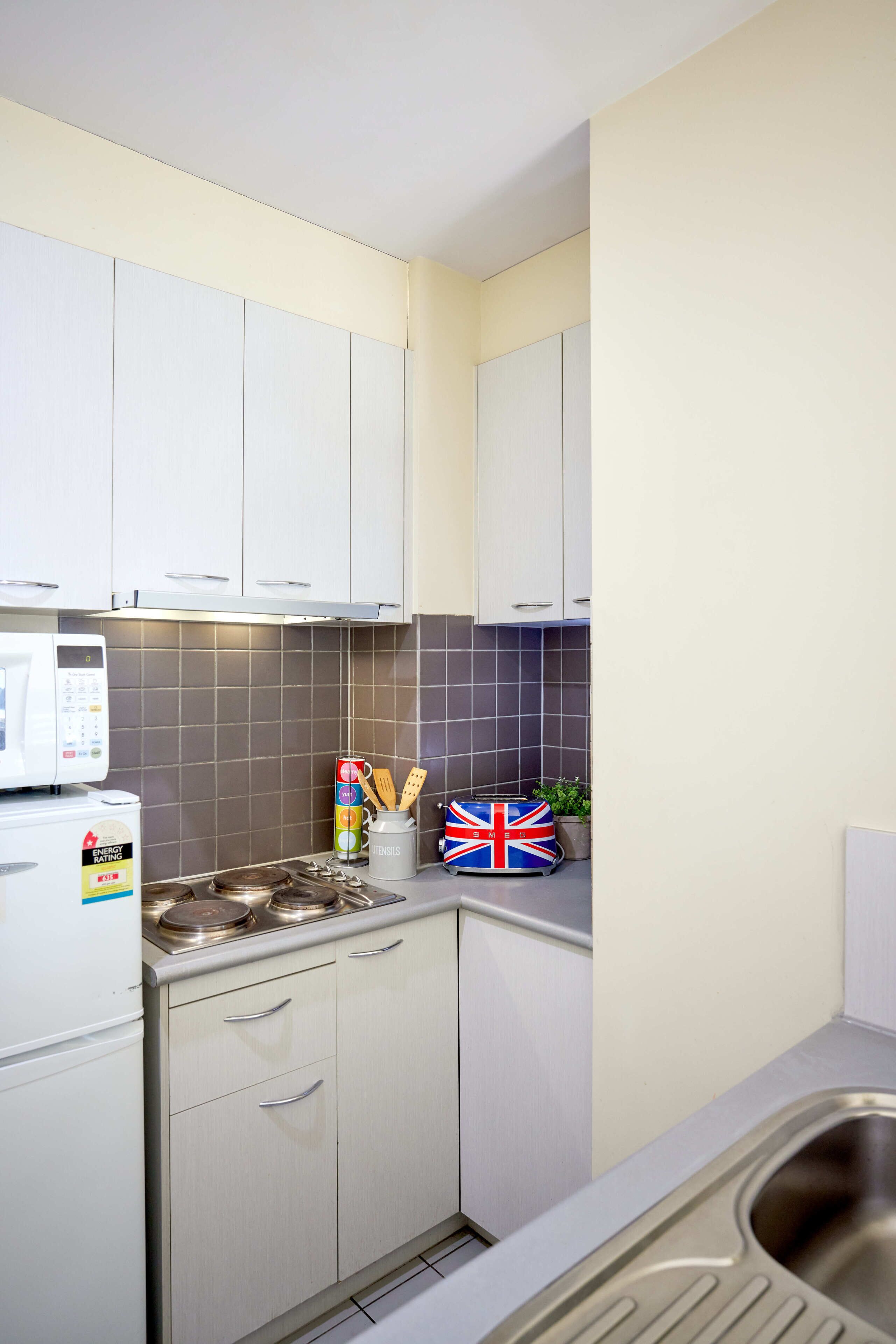 A compact kitchen with white cabinets, a microwave, a kettle, and a sink.