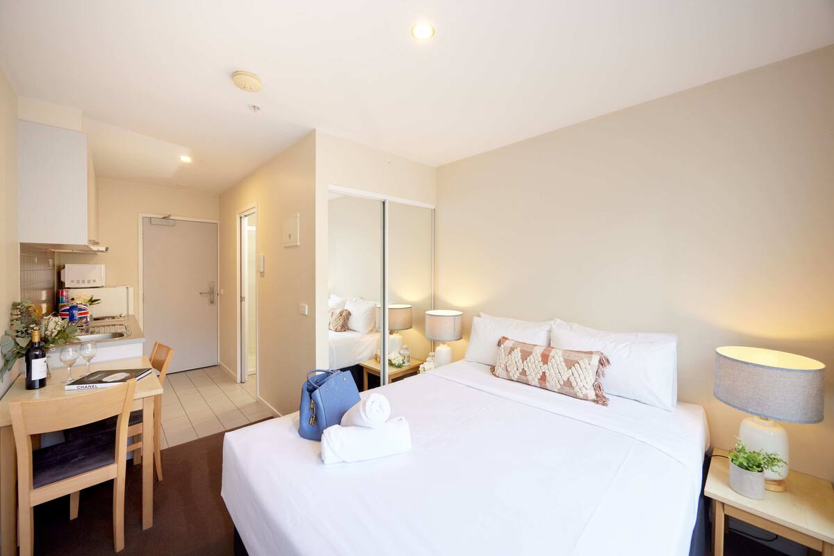 Una habitación de hotel con una cama, un escritorio con una silla, una mesita con una lámpara y un espejo.