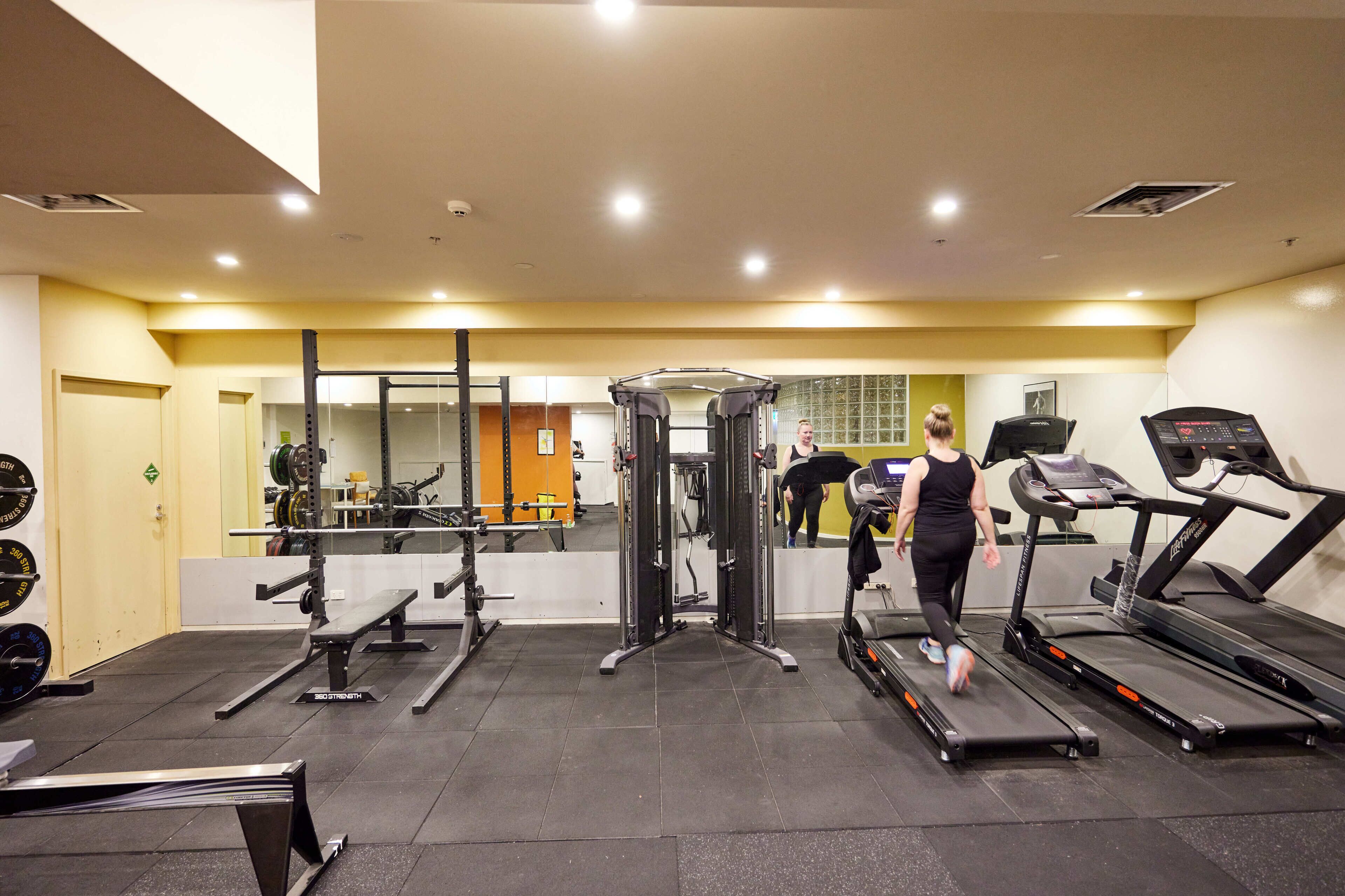 Ein Fitnessstudio mit Laufbändern, Krafttrainingsgeräten und einer Spiegelwand.