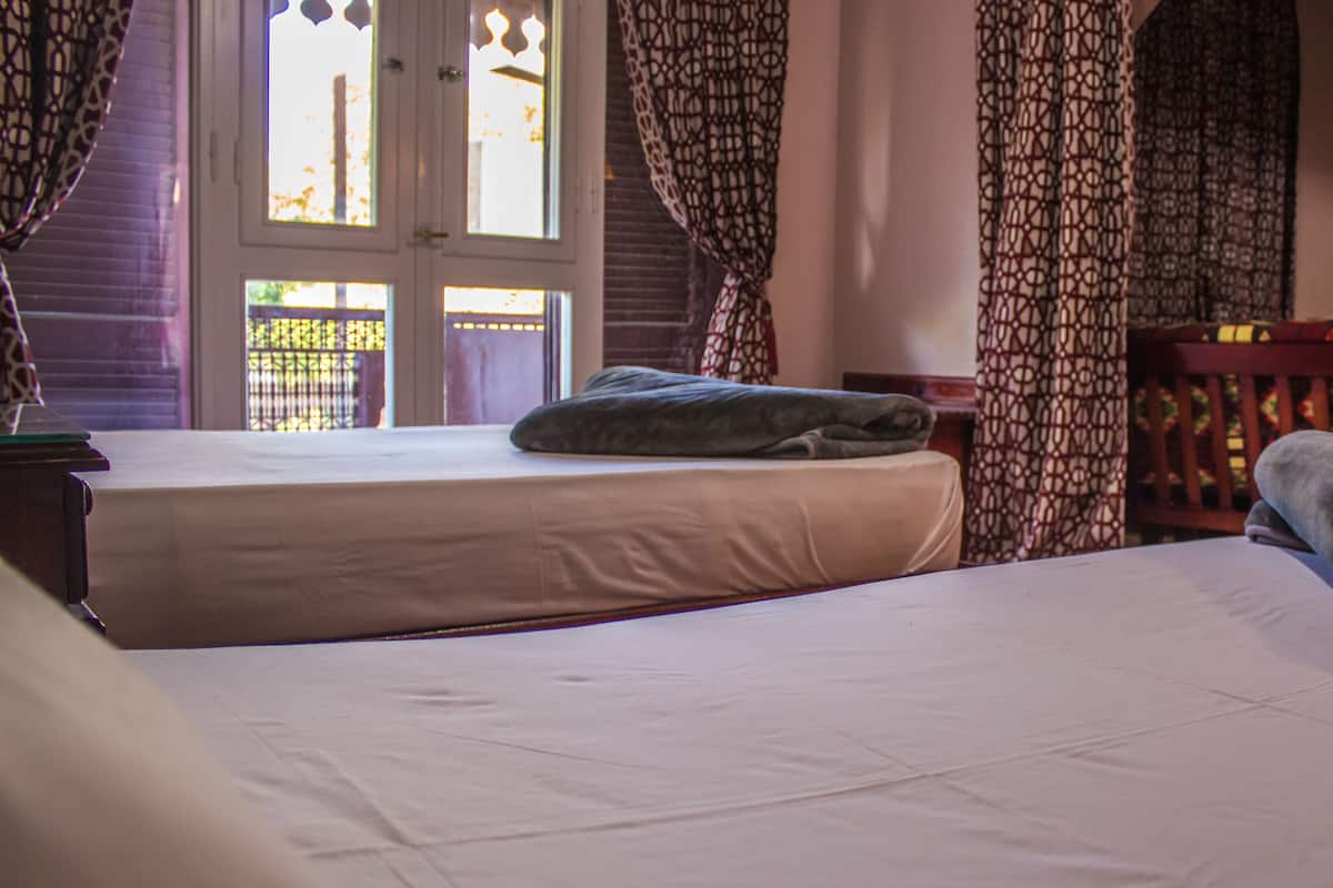 Quarto com duas camas, uma cabeceira de madeira e uma janela com cortinas estampadas.