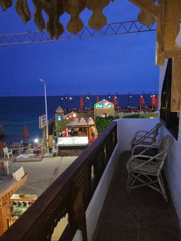 A balcony with wicker chairs, a view of the beach, and a restaurant named 'Bu Bu's' in the background.