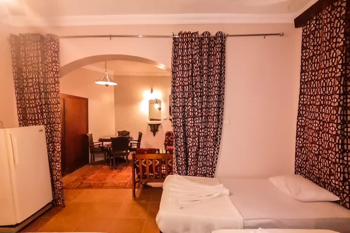 Quarto de hotel com duas camas, uma mesa de jantar, cadeiras, um frigorífico e cortinas estampadas.