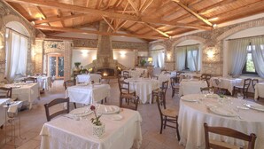 A restaurant with multiple tables set for dining, stone walls, and a high wooden ceiling. - Popilia Country Resort (Maierato)