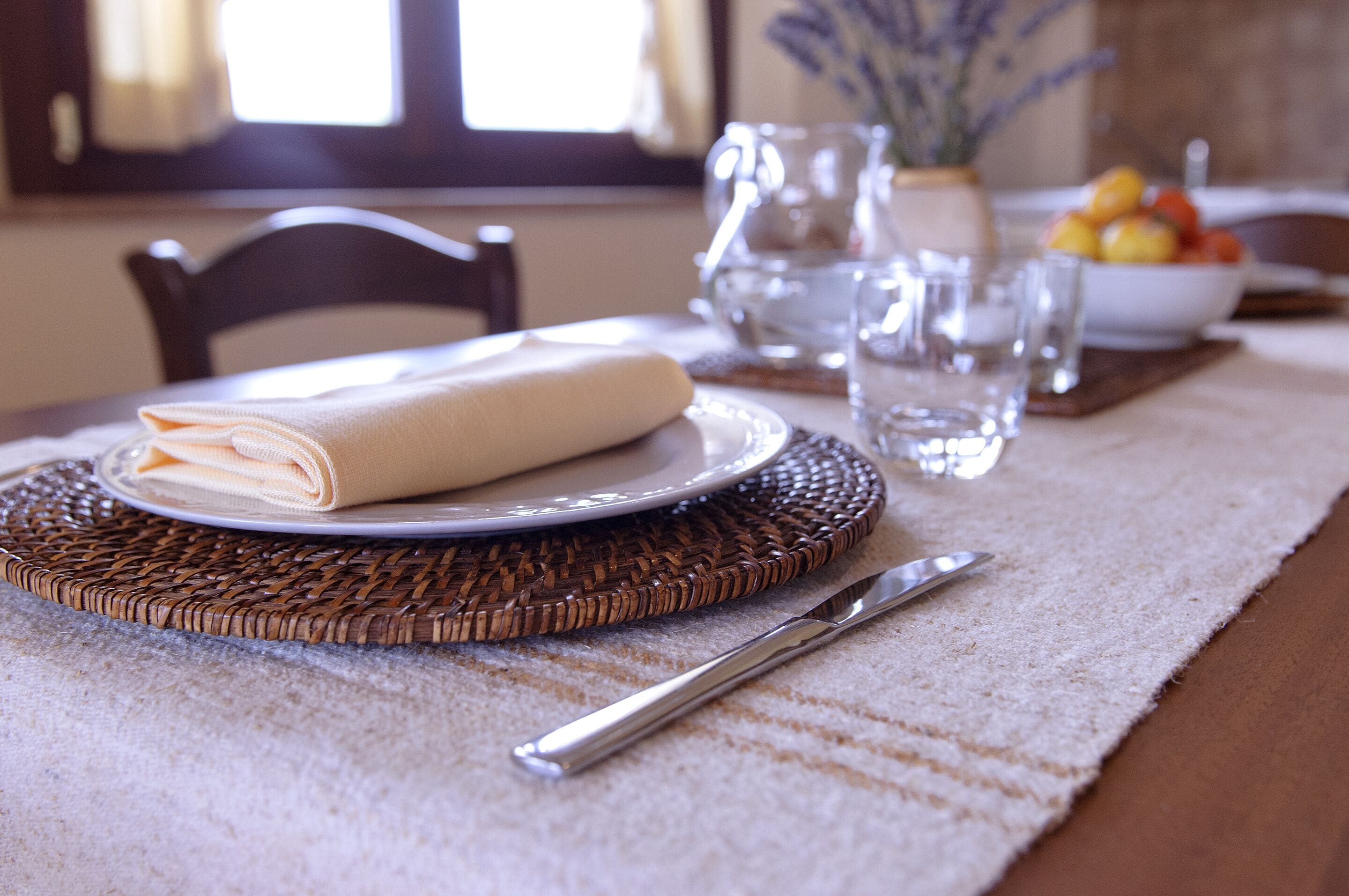 A dining table set with a folded napkin, a plate, a knife, and a bowl of fruit.
