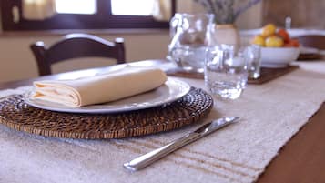 A dining table set with a folded napkin, a plate, a knife, and a bowl of fruit.