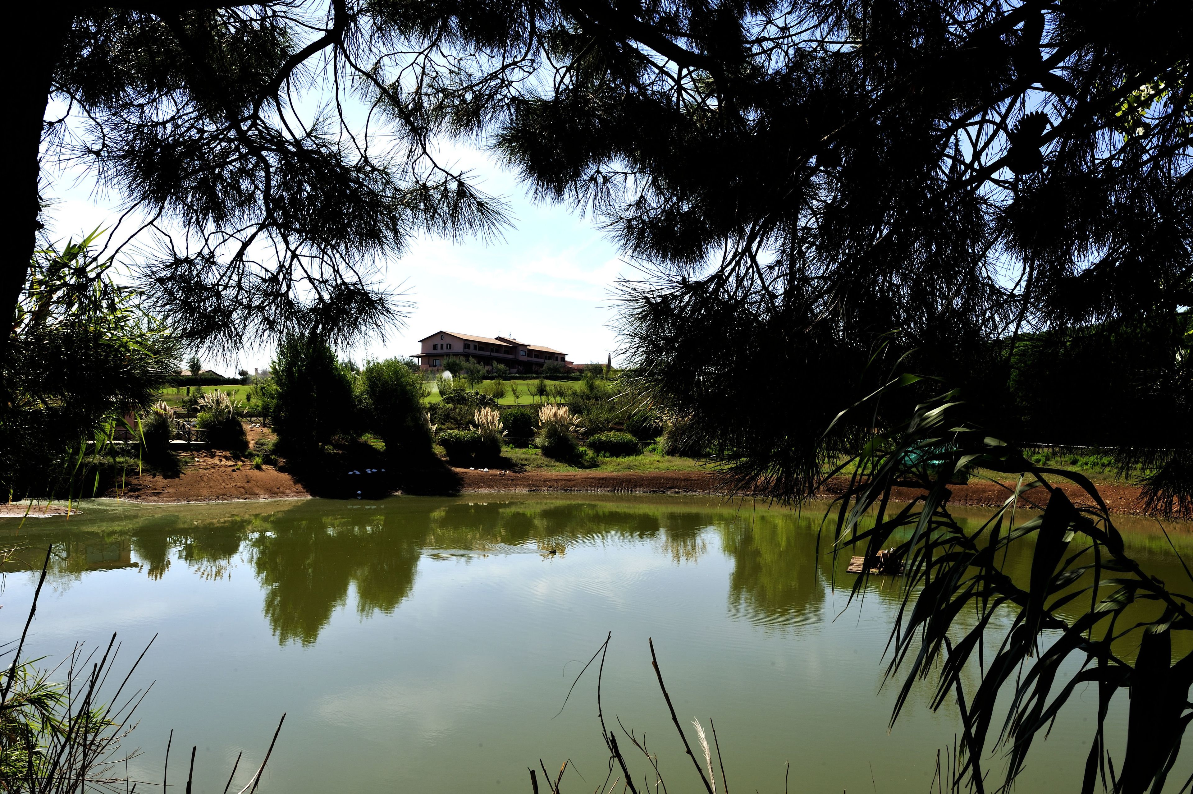 A serene landscape with a pond reflecting a building and trees.