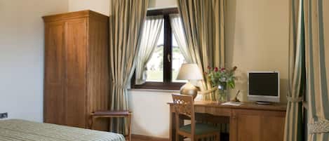 Un dormitorio con cama, escritorio con computadora, silla, armario de madera y ventana con cortinas.