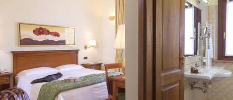 Habitación de hotel con cama, mesita de noche, lámpara, silla y baño con lavabo y espejo.