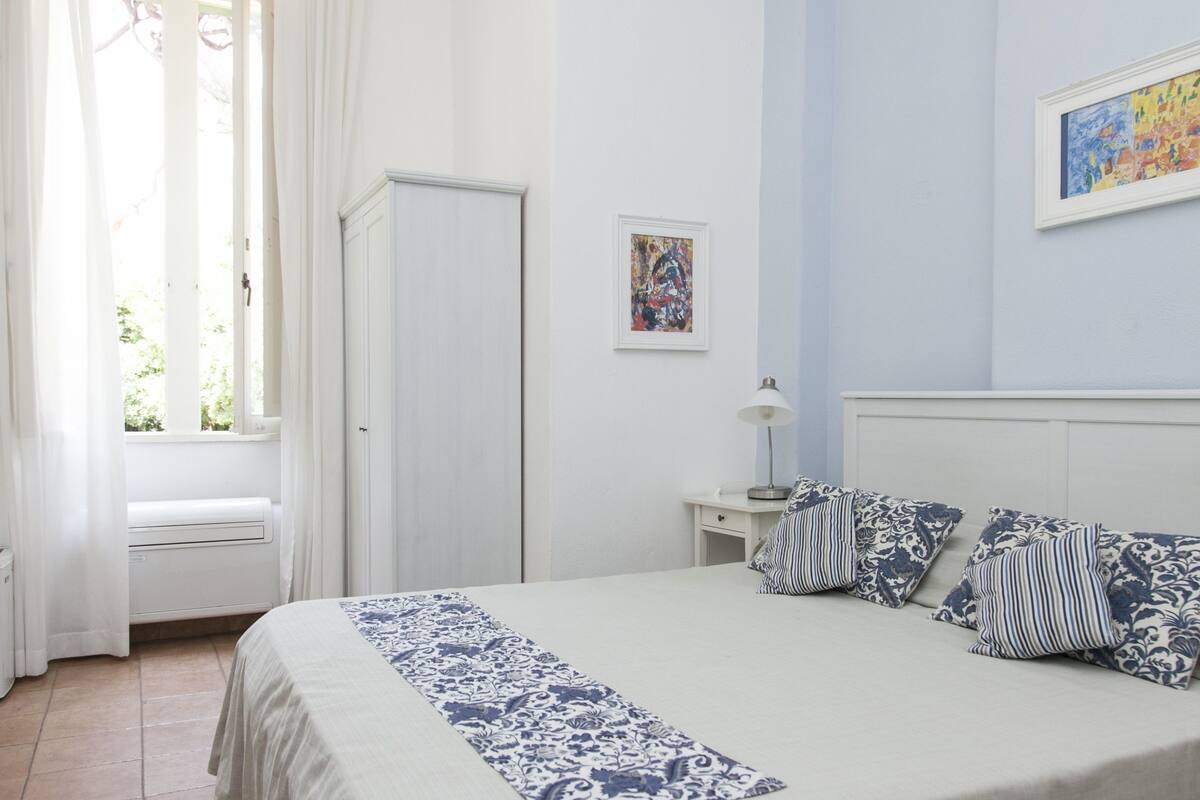 Une chambre à coucher avec un lit, une table de chevet, une lampe et deux œuvres d’art encadrées accrochées au mur.