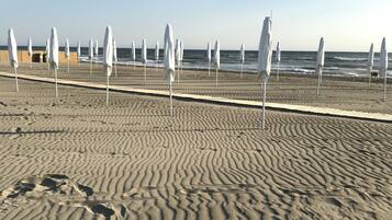 Una playa arenosa con hileras de sombrillas blancas y huellas en la arena.