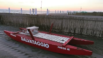 A red boat named 'SALVATAGGIO' on a sandy beach with a wooden fence and flags in the background.