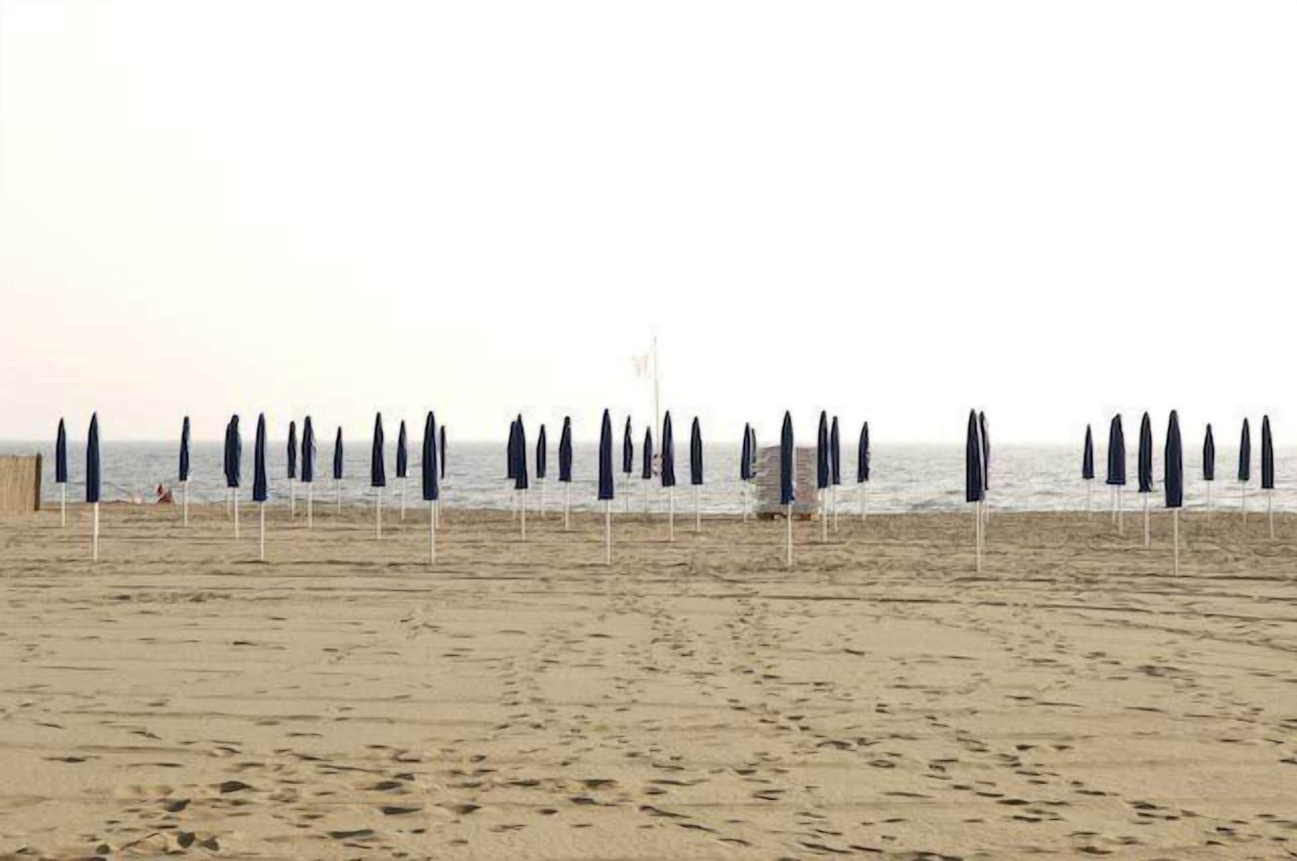 A beach with rows of umbrellas and a flagpole in the distance.