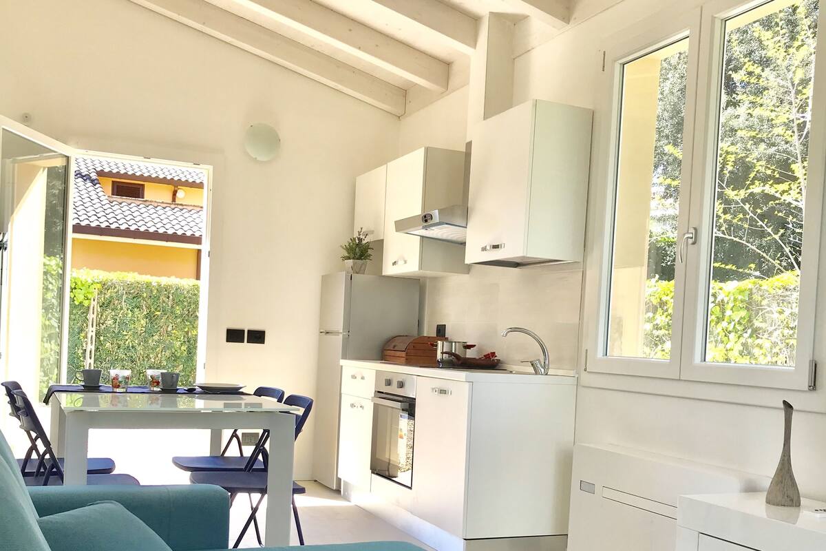 Une cuisine moderne avec des meubles blancs, un coin repas avec des chaises bleues et une grande fenêtre donnant sur un paysage verdoyant.