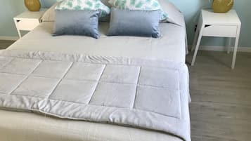 Una cama bien hecha con colcha, dos almohadas y dos mesitas de noche con lámparas.