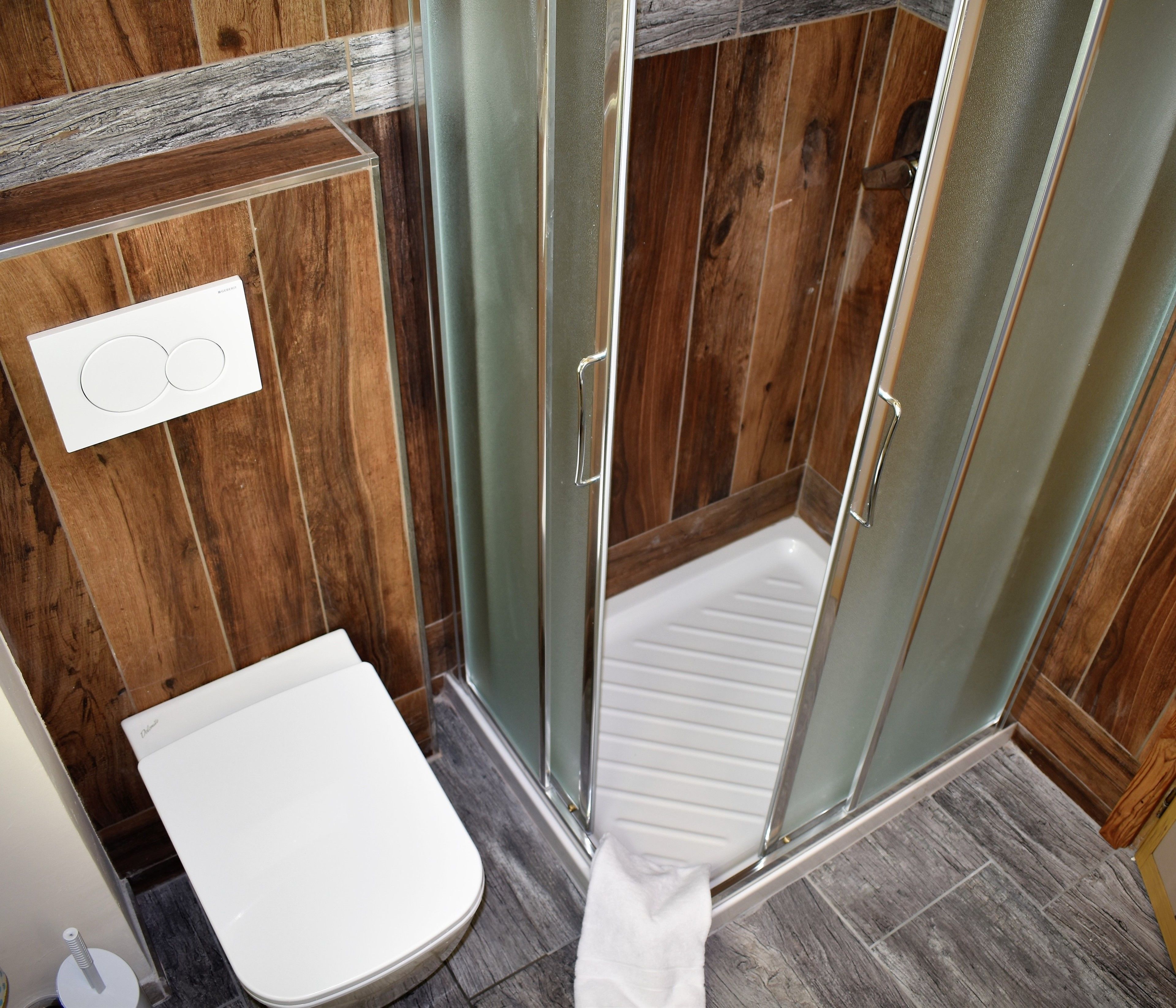 Eine Dusche mit Glastüren, eine weiße Toilette und eine Holzvertäfelung.