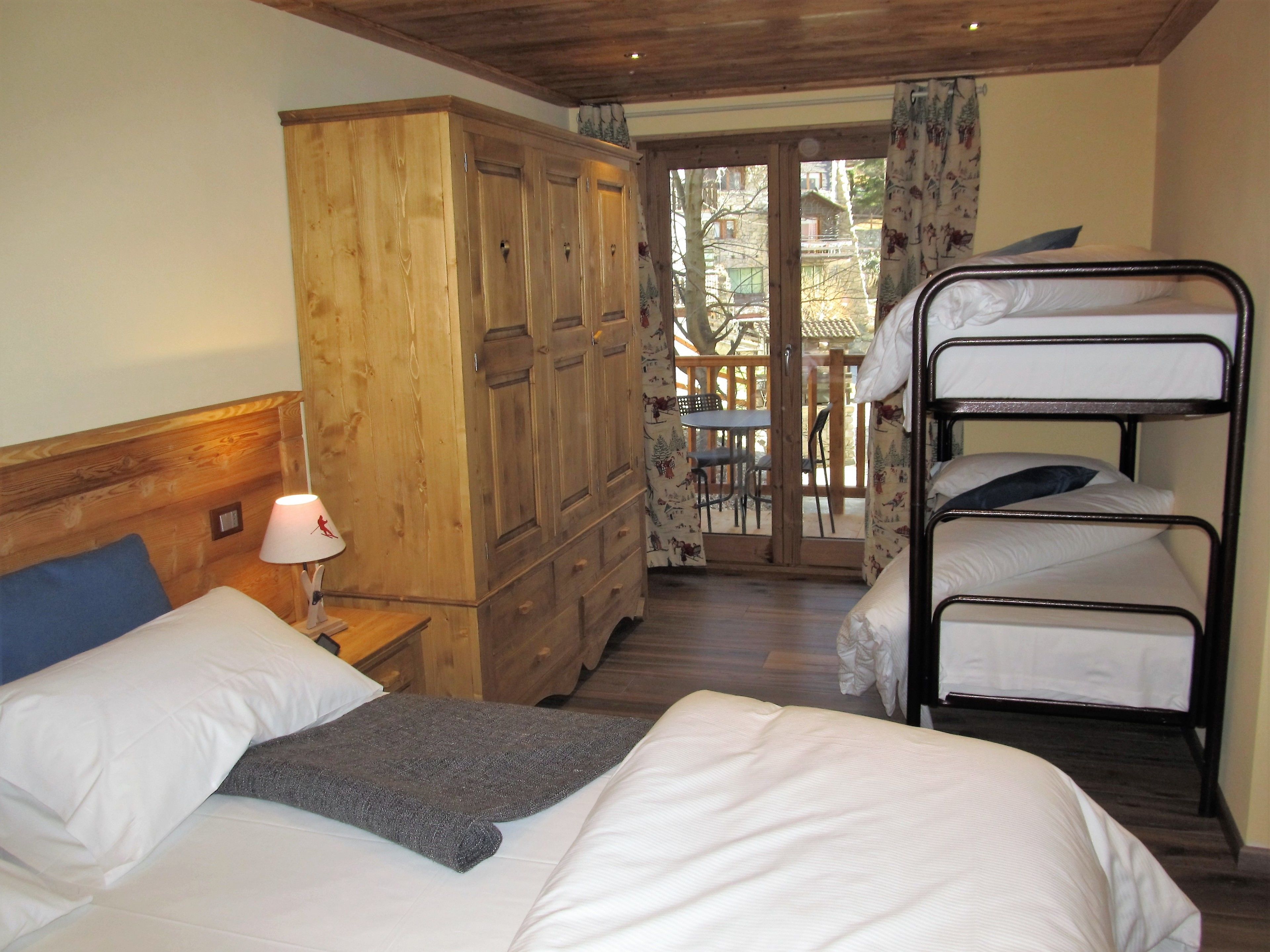 A room with a bed, a wardrobe, a desk with a lamp, and a bunk bed.