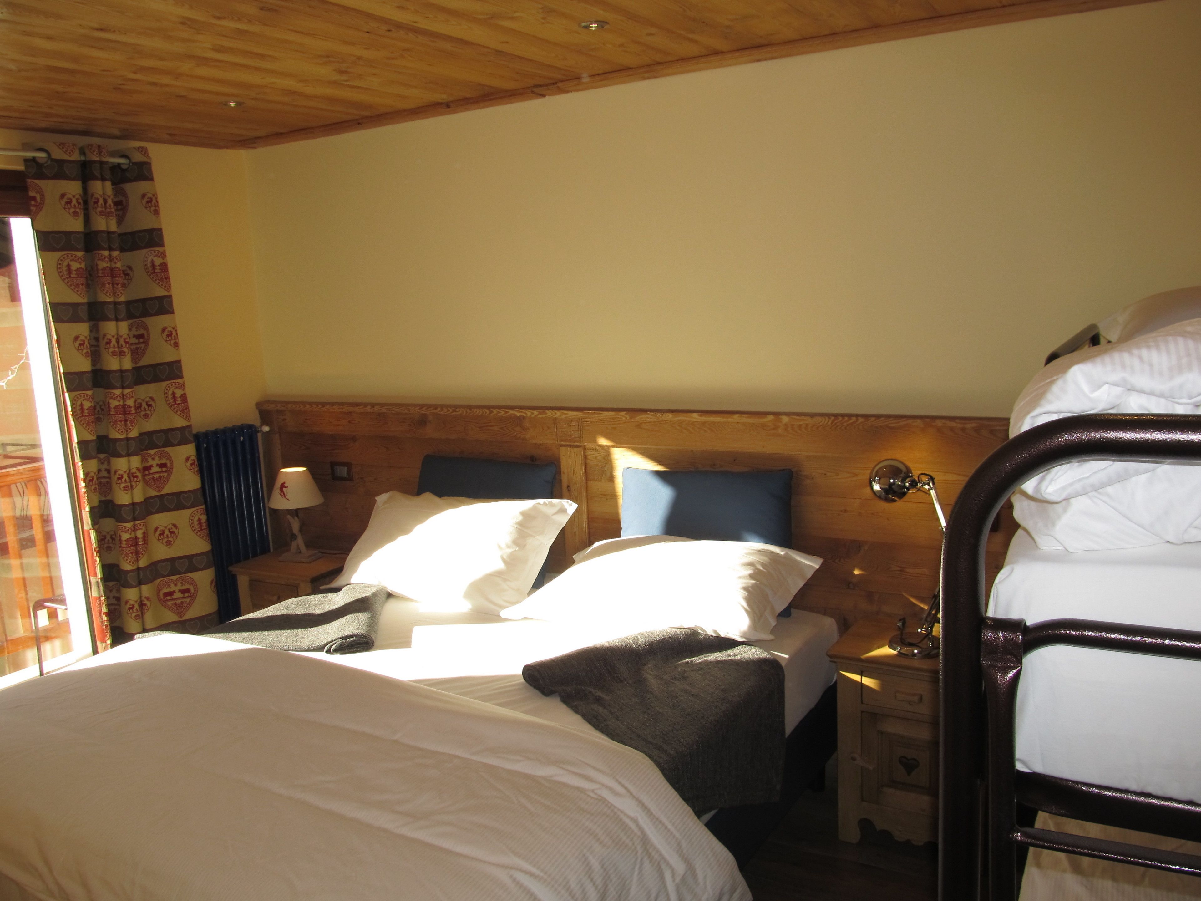 A room with a wooden headboard, two beds, a nightstand, a lamp, and a window with curtains.