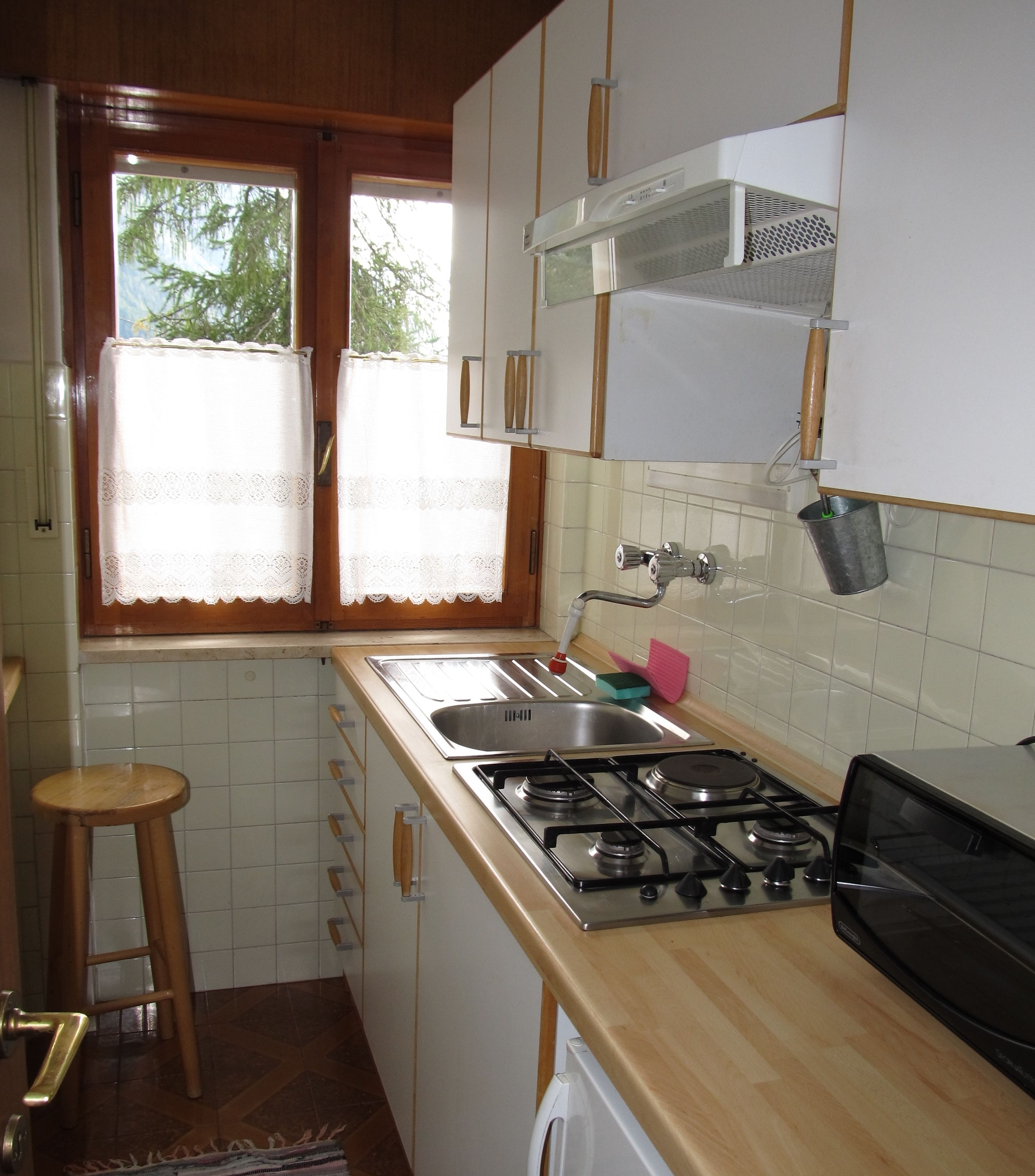 A compact kitchen with a gas stove, sink, and a window with lace curtains.