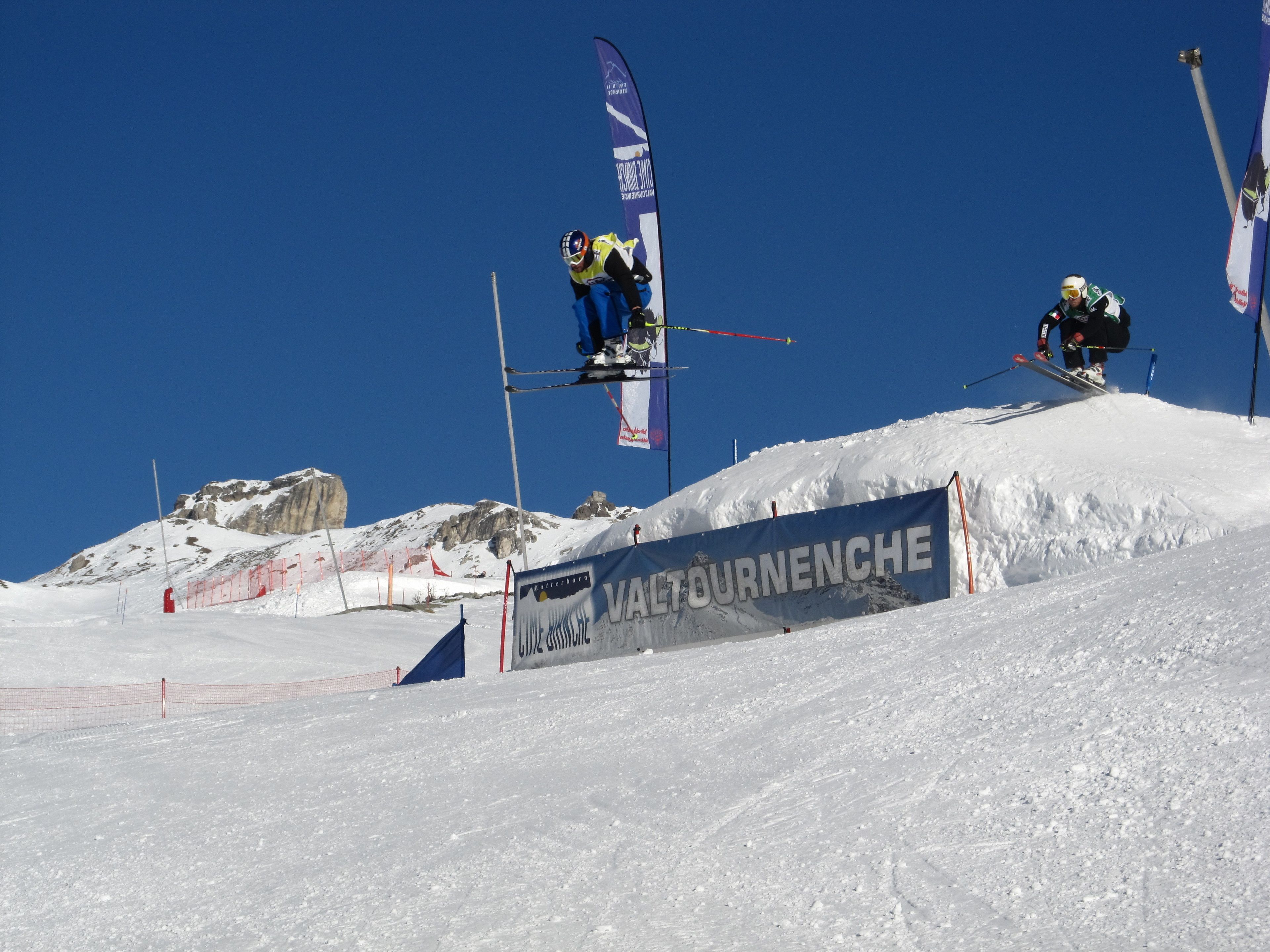 Eine Skisprungschanze mit einem Banner mit der Aufschrift 'VALTOURNENCHE' und einem strahlend blauen Himmel.