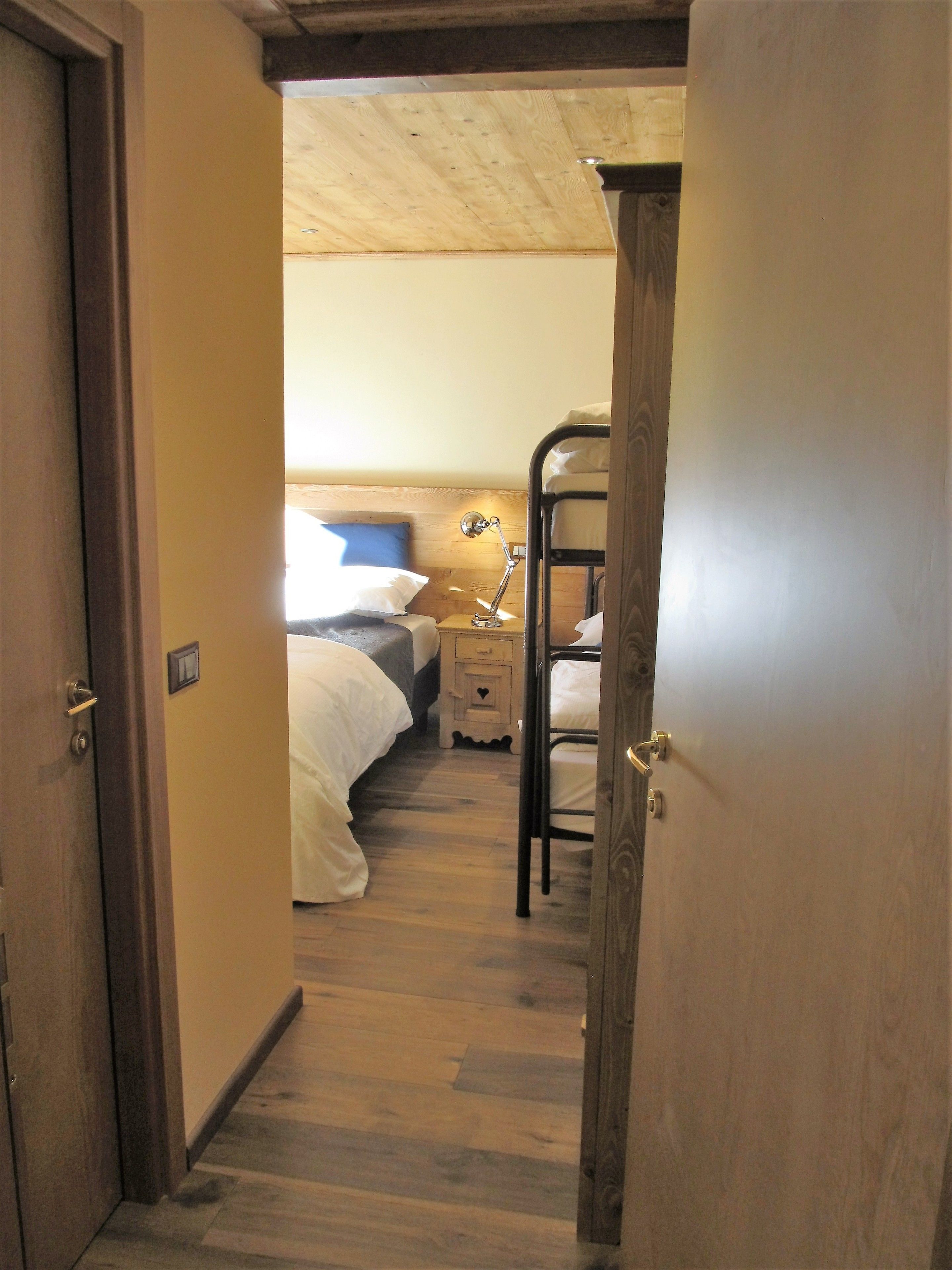 Un couloir étroit mène à une chambre où se trouve un lit superposé, une table de chevet avec une lampe et un plafond en bois.