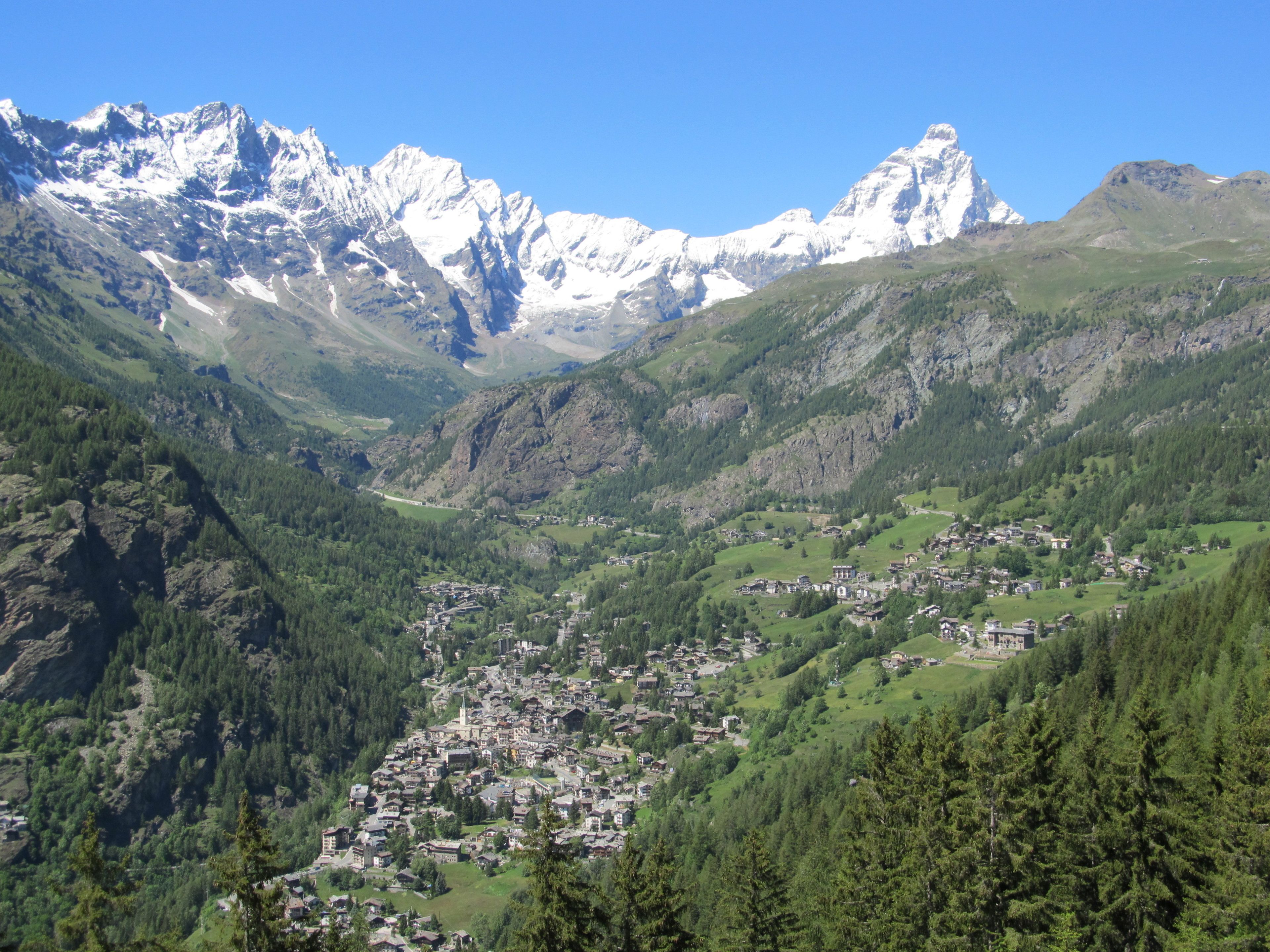 A mountainous landscape with a valley town featuring traditional buildings, a church, and a prominent mountain peak in the background.