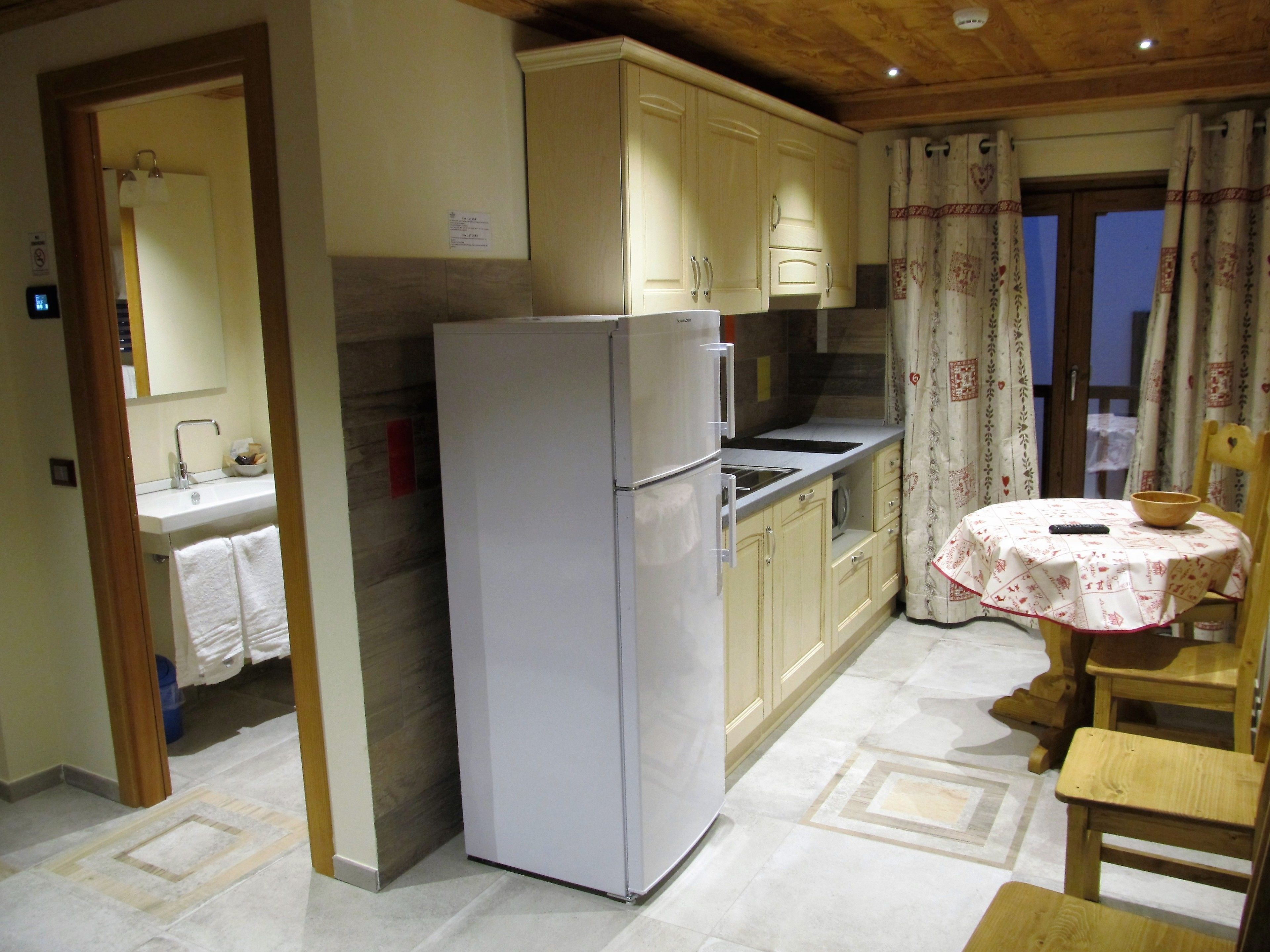 A kitchen with a refrigerator, cabinets, a sink, and a dining area with a table and chairs.