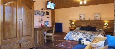 Un dormitorio con un armario de madera, un escritorio, una silla, una cama con ropa de cama estampada y un televisor en la pared.