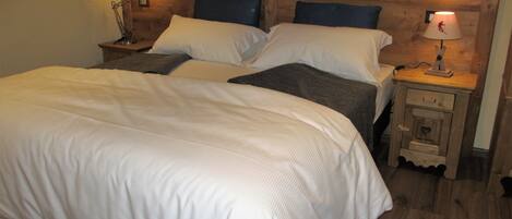 Una cama doble con ropa de cama blanca, dos mesitas de noche con lámparas y un cabecero de madera.