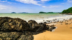 A beach with rocky foreground, clear turquoise water, and distant islands.