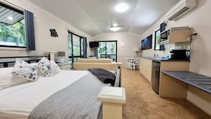 A compact hotel room with a bed, bedside table, lamp, and a view of the outdoors.
