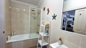 A bathroom with a glass-enclosed shower, a white bathtub, and a white shelf with toiletries. - Boutique Bungalows (Wongaling Beach)