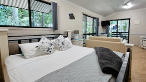 A hotel room with a bed, a sofa, a TV, and large windows with a view of trees.