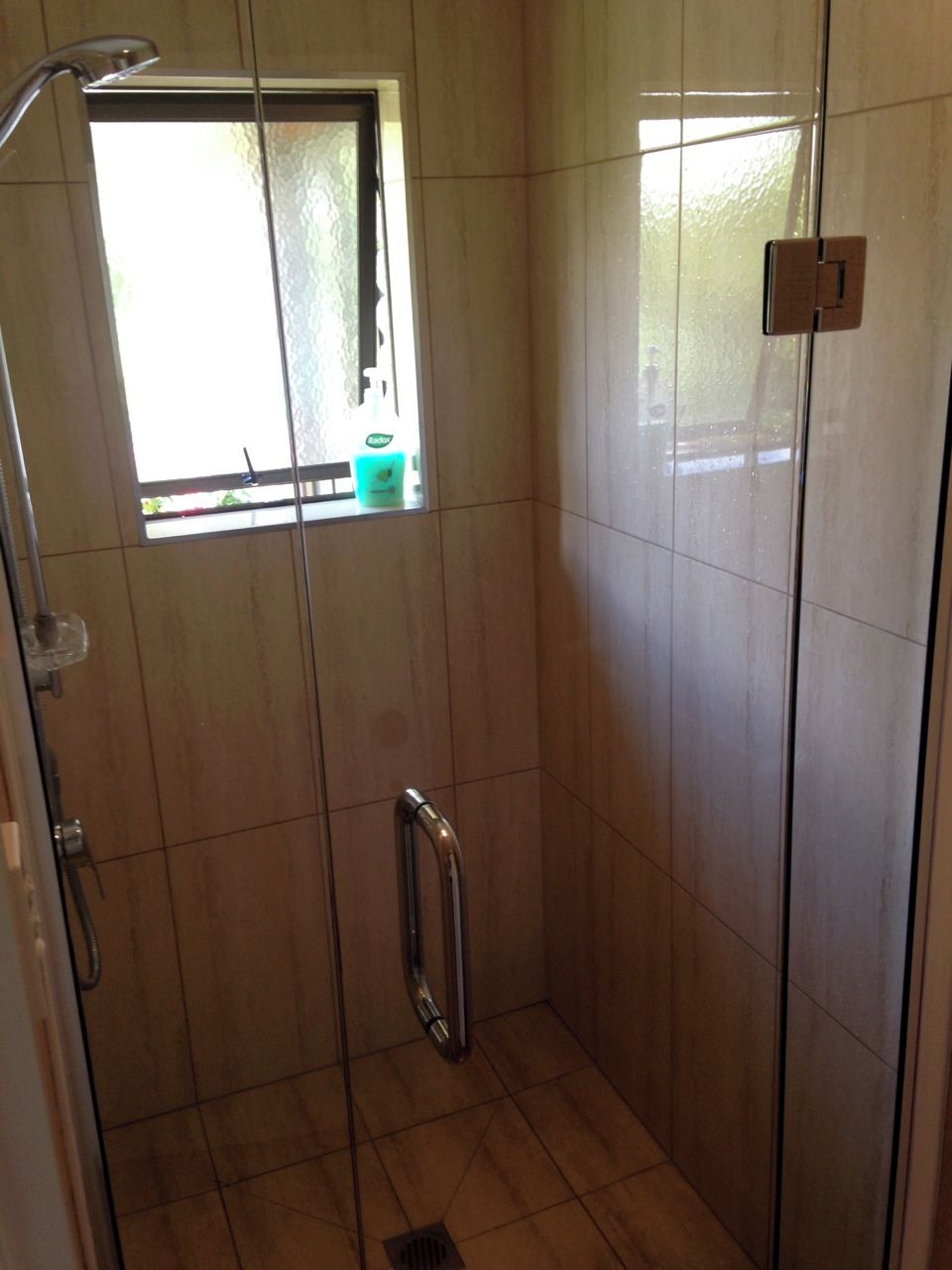 Un área de ducha pequeña y cerrada, con ventana, un perchero y una puerta.