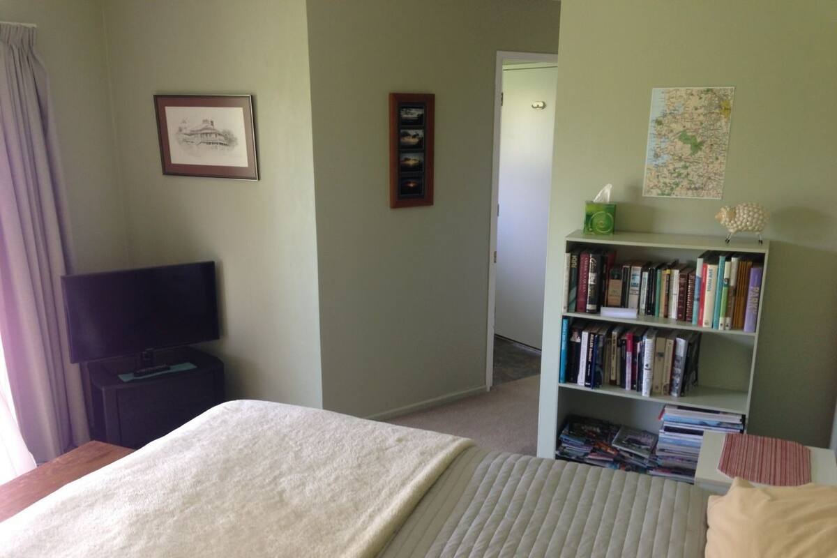 A hotel room with a bed, a bookshelf, a television, and a map on the wall.