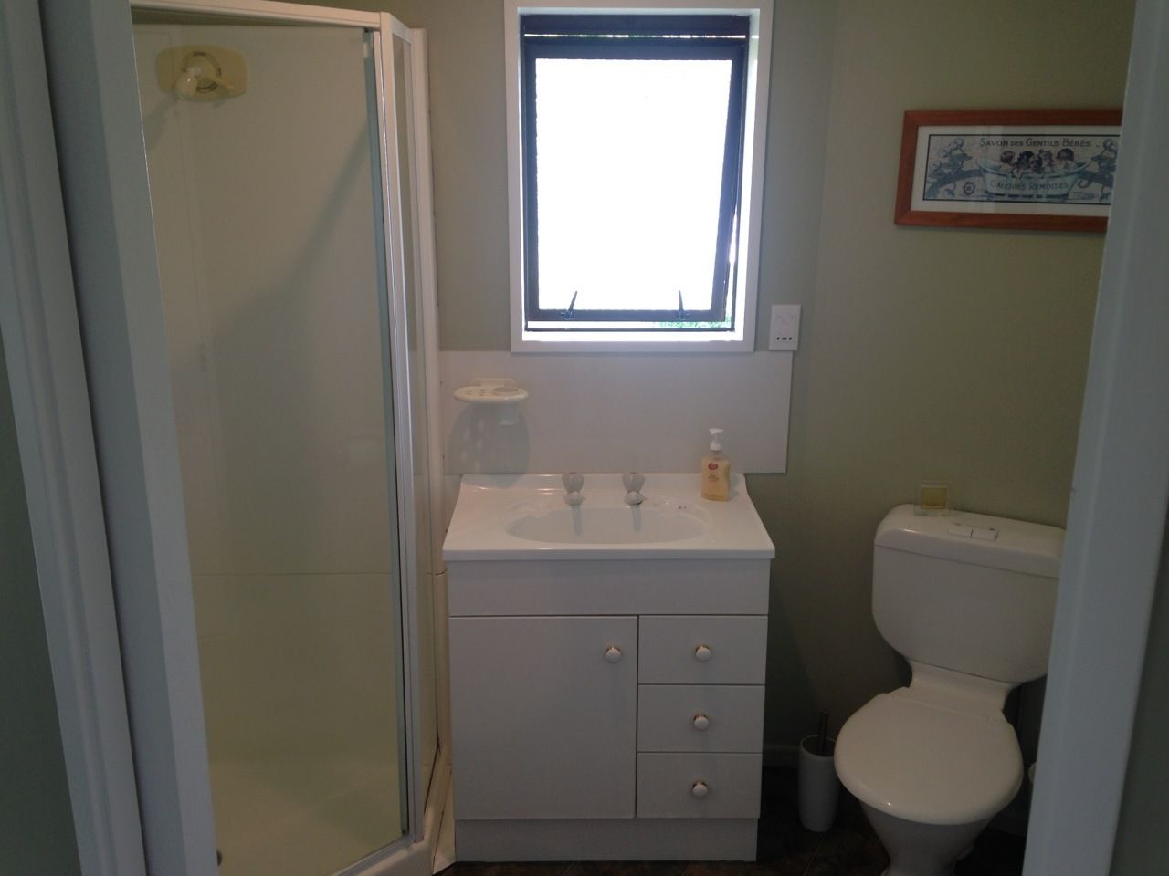 Un baño con un lavabo blanco, dos grifos, un inodoro y una ventana sobre el lavabo.