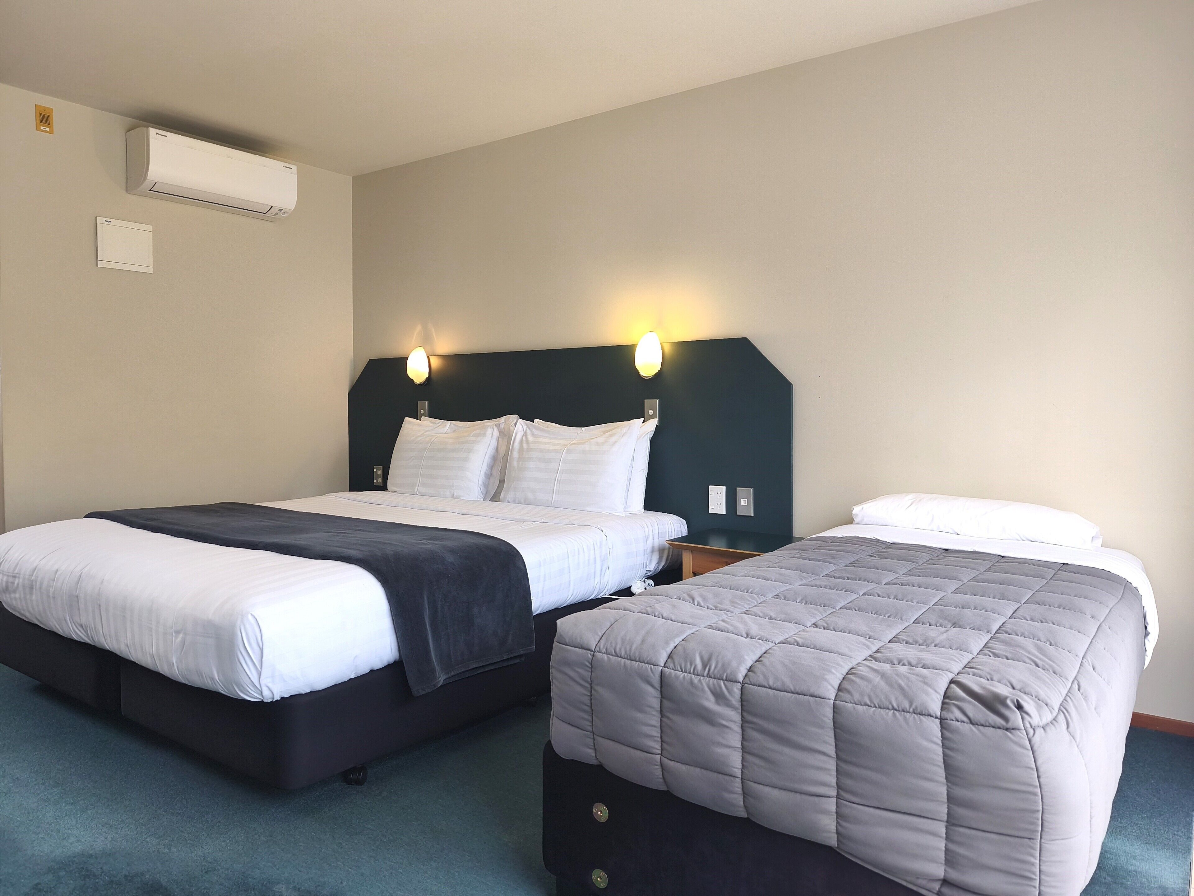 Habitación de hotel con dos camas, cabecera oscura, aire acondicionado instalado en la pared y lámparas de noche.